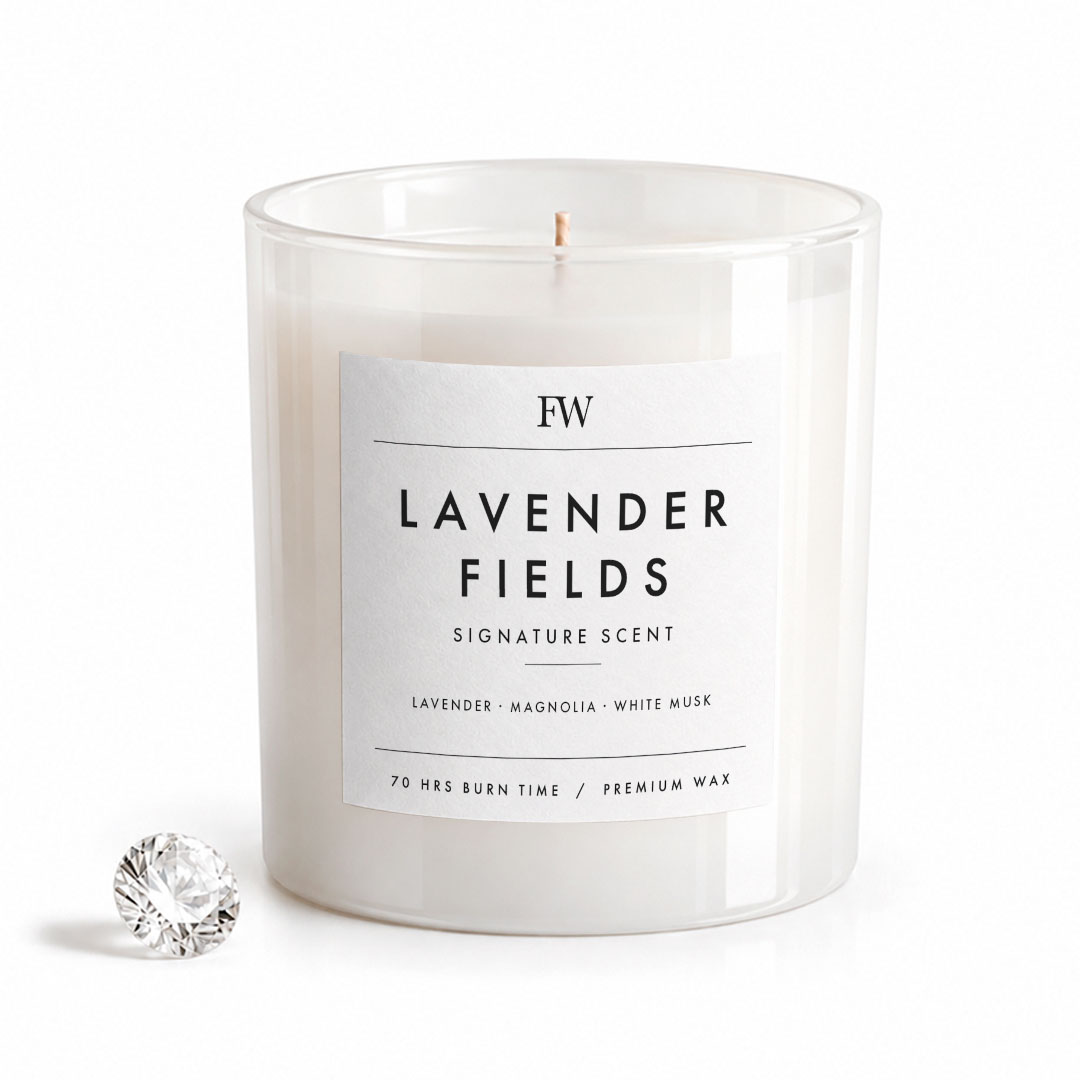 A clear glass jar candle with white wax and a white label reading 'FW LAVENDER FIELDS SIGNATURE SCENT' on a clean white background, with a small faceted clear stone prop beside it.