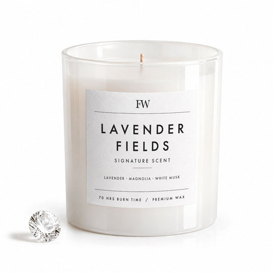 A clear glass jar candle with white wax and a white label reading 'FW LAVENDER FIELDS SIGNATURE SCENT' on a clean white background, with a small faceted clear stone prop beside it.